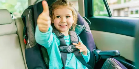 Uśmiechnięte dziecko w foteliku samochodowym pokazuje kciuk w górę. Bezpieczna podróż to podstawa!