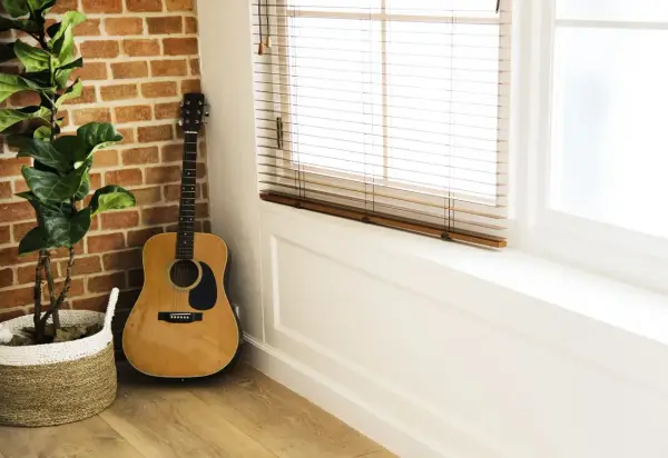 Gitara akustyczna obok ceglanej ściany i rośliny w koszu. Idealne miejsce na naukę piosenki na gitarę dla początkujących dzieci.
