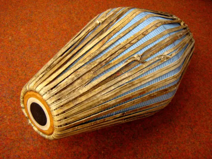 Mridanga, jeden z najstarszych instrumentów muzycznych, z niebieską membraną i drewnianymi wzmocnieniami, leży na pomarańczowym tle.